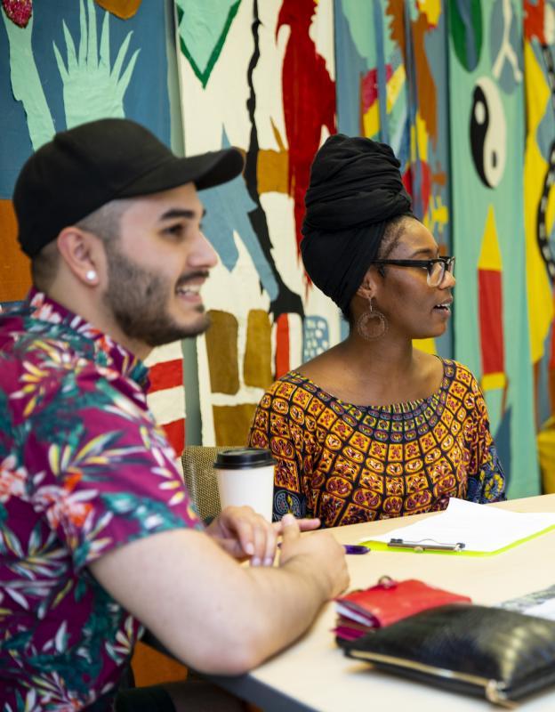 two students in front of a painted wall facing and chatting with friends to the right of camera's view